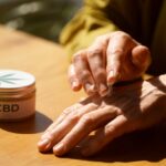 Hands applying CBD Creams for Eczema from a jar, placed on a wooden surface.