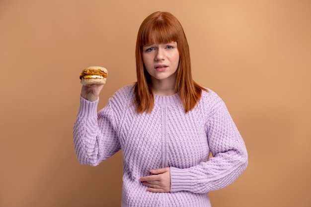 Woman holding a burger, experiencing hunger and discomfort, discussing How to Stop Menopause Hunger.