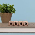 Wooden blocks spelling "ADHD" on a book, raising the question: Can a Primary Care Physician Prescribe Adderall?